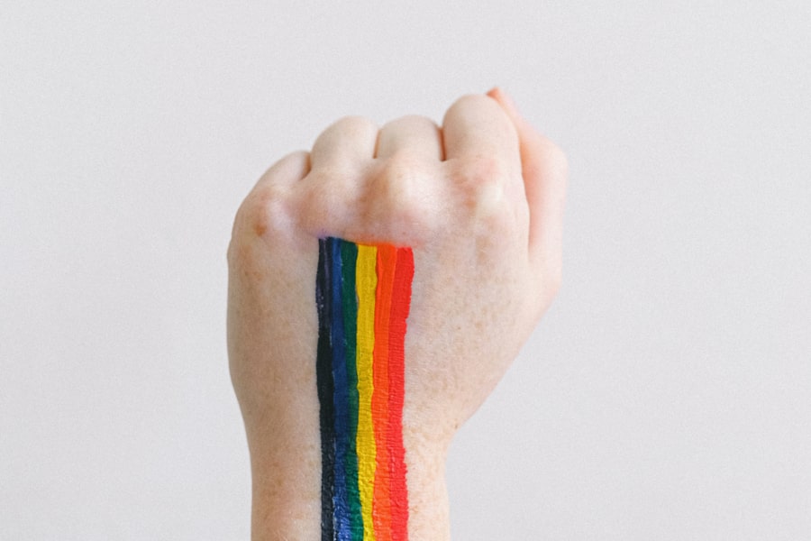Fist with the pride rainbow colours painted on, in front of a light grey background