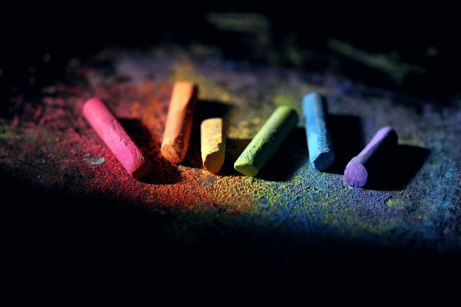 Chalk crayons of the pride rainbow colours left on a dark and dusty floor .