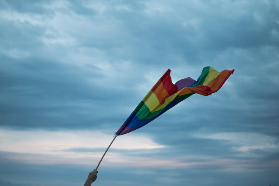Pride flag being held in the air and waving in the wind in front of a moody evening sky.